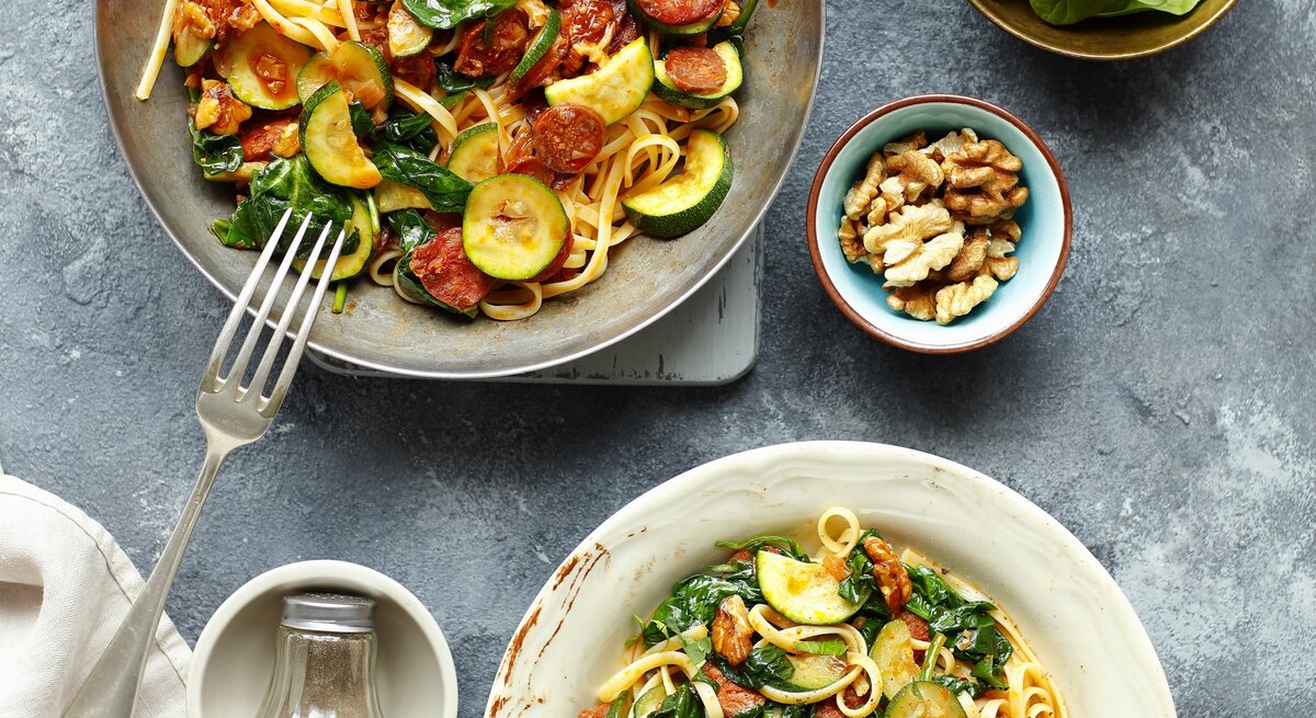 Linguine mit Chorizo und Zucchini auf eine grauen Telle ru ddunklem Tisch direkt von oben fotografiert.