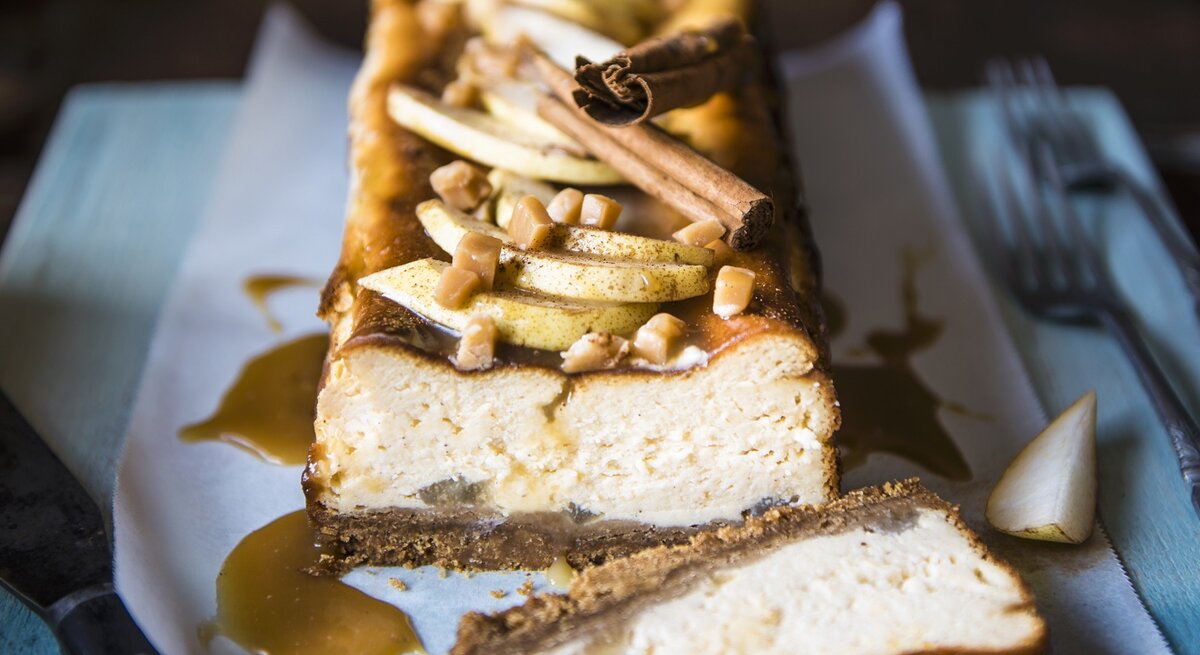 Der Toffee-Birnen-Käsekuchen angeschnitten auf einer bläulichen Serviette von vorne fotografiert.