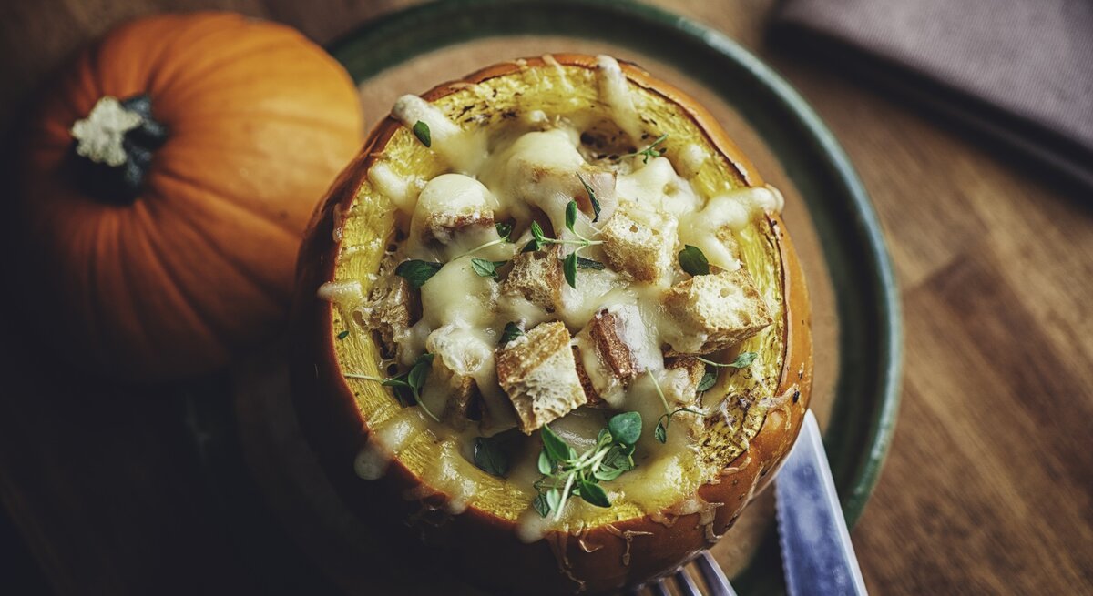 Draufsicht auf einen gefüllten Kürbis mit Kürbissuppe, überbacken mit Hackfleisch und Käse auf Holztisch. 