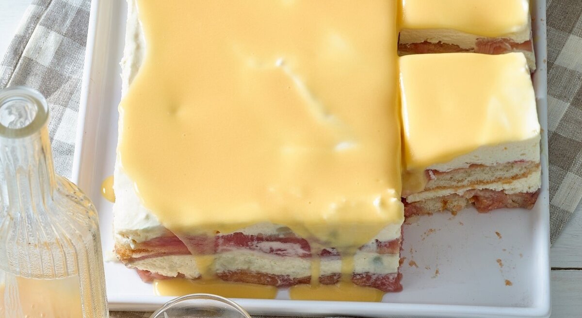 Draufsicht: Zwei angeschnittene gelbe Tiramisu mit Eierlikör auf einem Tisch. Davor steht eine Glasflasche, die mit einer hellen Flüssigkeit gefüllt ist.