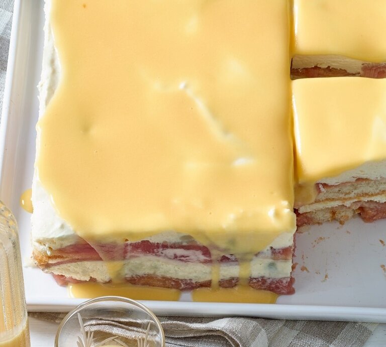 Draufsicht: Zwei angeschnittene gelbe Tiramisu mit Eierlikör auf einem Tisch. Davor steht eine Glasflasche, die mit einer hellen Flüssigkeit gefüllt ist. | © Matthias Liebich