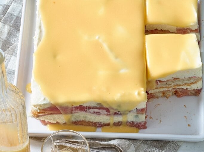 Draufsicht: Zwei angeschnittene gelbe Tiramisu mit Eierlikör auf einem Tisch. Davor steht eine Glasflasche, die mit einer hellen Flüssigkeit gefüllt ist. | © Matthias Liebich