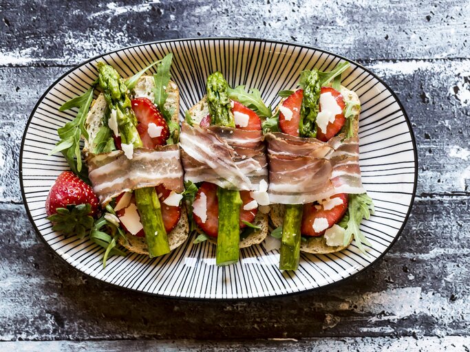 Bruschetta belegt mit Spargel, Erdbeeren, Rucola, Parmaschinken und Parmesan. | © Getty Images/ Westend61