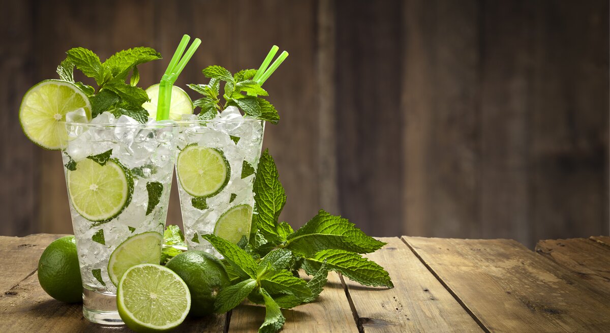 Zwei mit Minze dekorierte Gläser gefüllt mit klassischem Mojito-Cocktail in hölzerner Kulisse. 