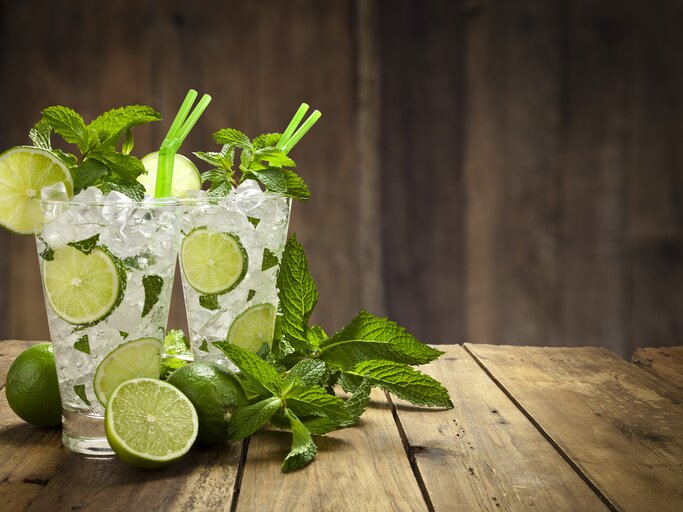 Zwei mit Minze dekorierte Gläser gefüllt mit klassischem Mojito-Cocktail in hölzerner Kulisse.  | © iStock/fcafotodigital