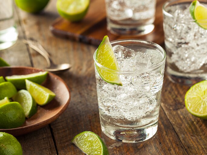 Glas mit prickelnder, durchsichtiger Flüssigkeit (Gin Tonic) dekortiert mit Limette auf Holztisch | © iStock/bhofack2