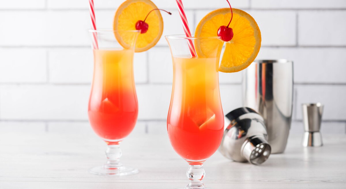Zwei mit einer Orangenscheibe dekortiere Cocktails mit einem Farbverlauf von Rot zu Gelb, was an einen Sonnenaufgang erinnert. 