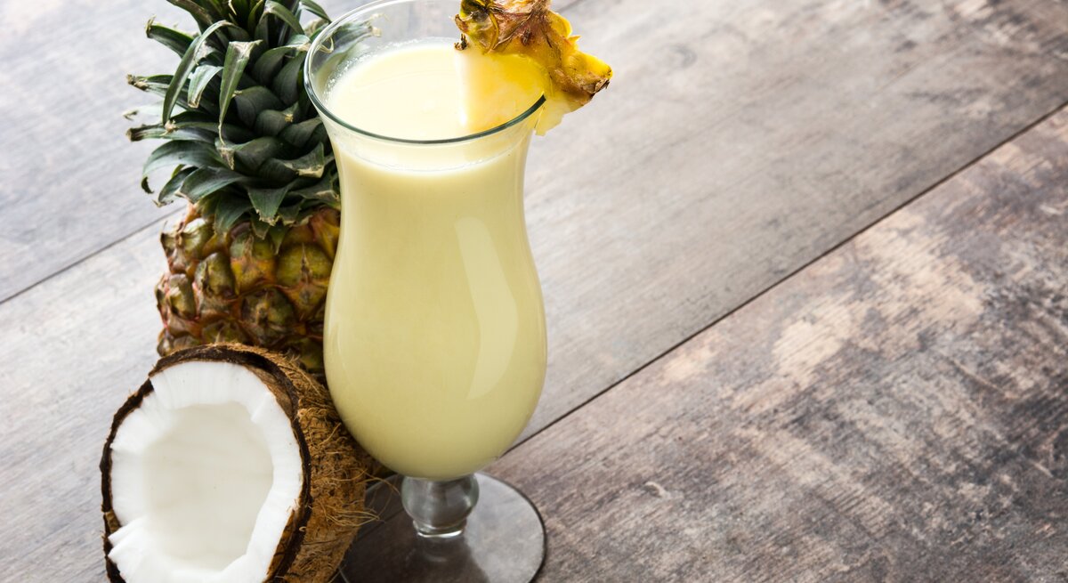 Ein mit Ananas dekoriertes Glas mit cremiger Piña Colada auf Holztisch. 