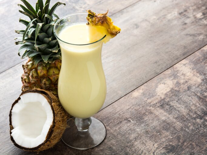 Ein mit Ananas dekoriertes Glas mit cremiger Piña Colada auf Holztisch.  | © iStock/etorres69