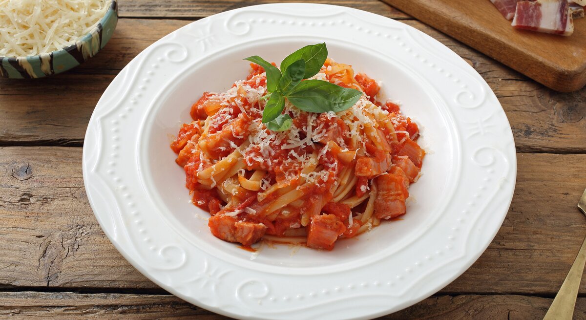 Teller mit Pasta in Tomatensoße, bestreut mit geriebenem Käse und gekrönt mit einem frischen Basilikumblatt, serviert auf einem rustikalen Holztisch. 