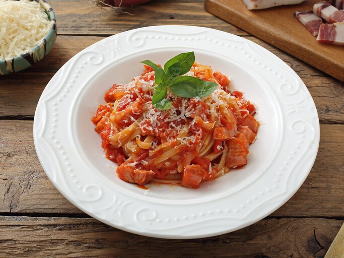 Teller mit Pasta in Tomatensoße, bestreut mit geriebenem Käse und gekrönt mit einem frischen Basilikumblatt, serviert auf einem rustikalen Holztisch.  | © iStock/ DENIO RIGACCI