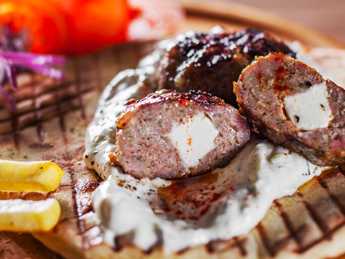 Angeschnittenes, griechisches Hacksteak "Bifteki" mit Feta-Füllung. Darunter ein Fladenbrot, daneben Pommes Frites.  | © iStock/semenovp