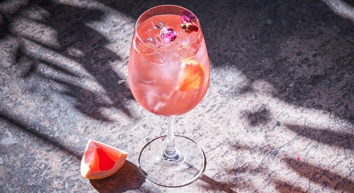 Ein Glas Pink Spritz auf ein er Betonfläche von schräg oben fotografiert.