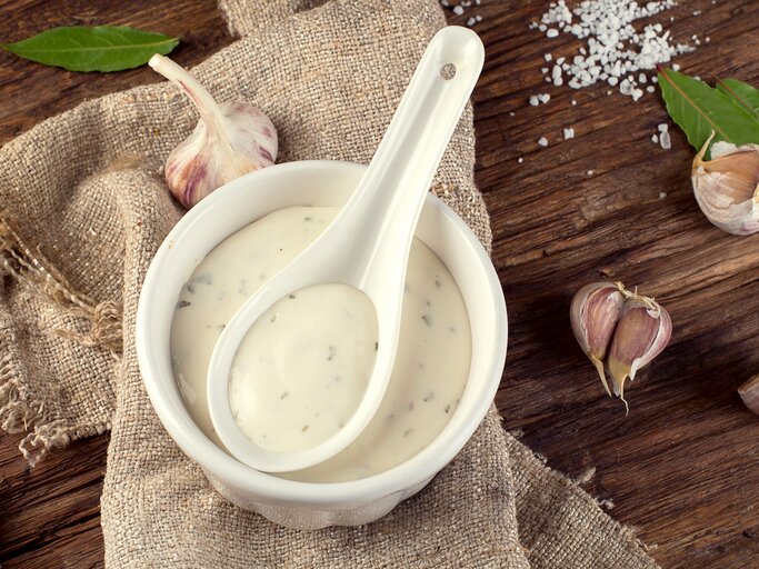 Weiße Schale mit einer cremigen Aioli mit Kräutern auf einem Holzbrett. | © iStock.com/bit245