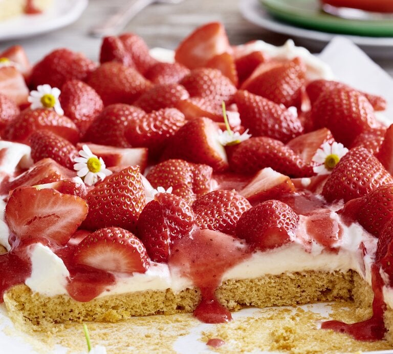 Der angeschnittene Erdbeer-Kuchen in der Nahaufnahmen mit Frühlingsblumen.  | © EAT CLUB/ Isabell Triemer