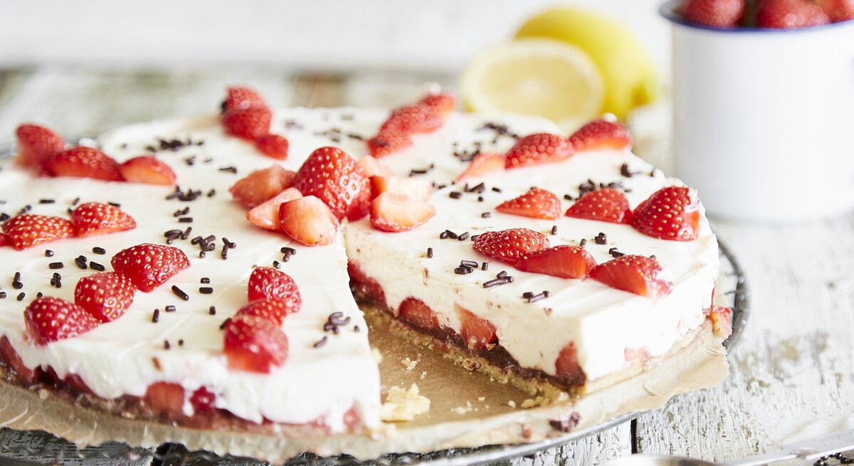 Ansprechende Erdbeertorte mit weißer Creme und dunklen Schokoladenstreuseln, präsentiert auf Holzuntergrund.