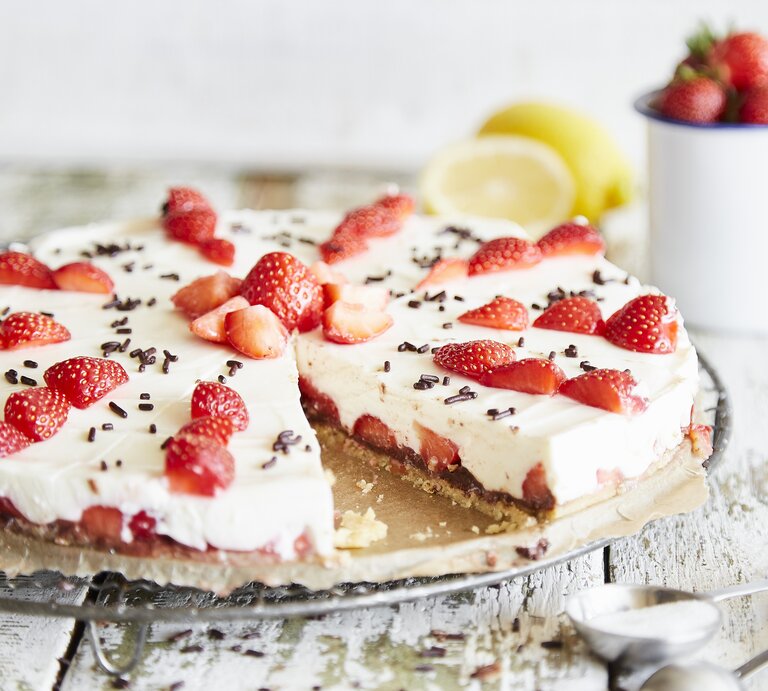 Ansprechende Erdbeertorte mit weißer Creme und dunklen Schokoladenstreuseln, präsentiert auf Holzuntergrund. | © StockFood / Springlane