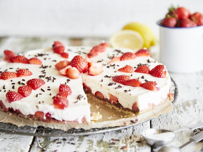 Ansprechende Erdbeertorte mit weißer Creme und dunklen Schokoladenstreuseln, präsentiert auf Holzuntergrund. | © StockFood / Springlane