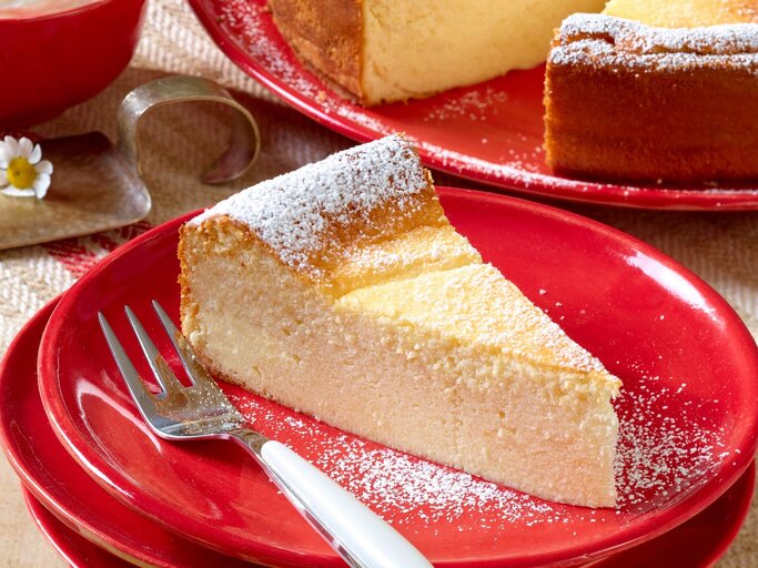 Ein Stück Käsekuchen auf einem roten Teller und hellem Holztisch. Alles von schräg oben fotografiert. | © Matthias Liebich