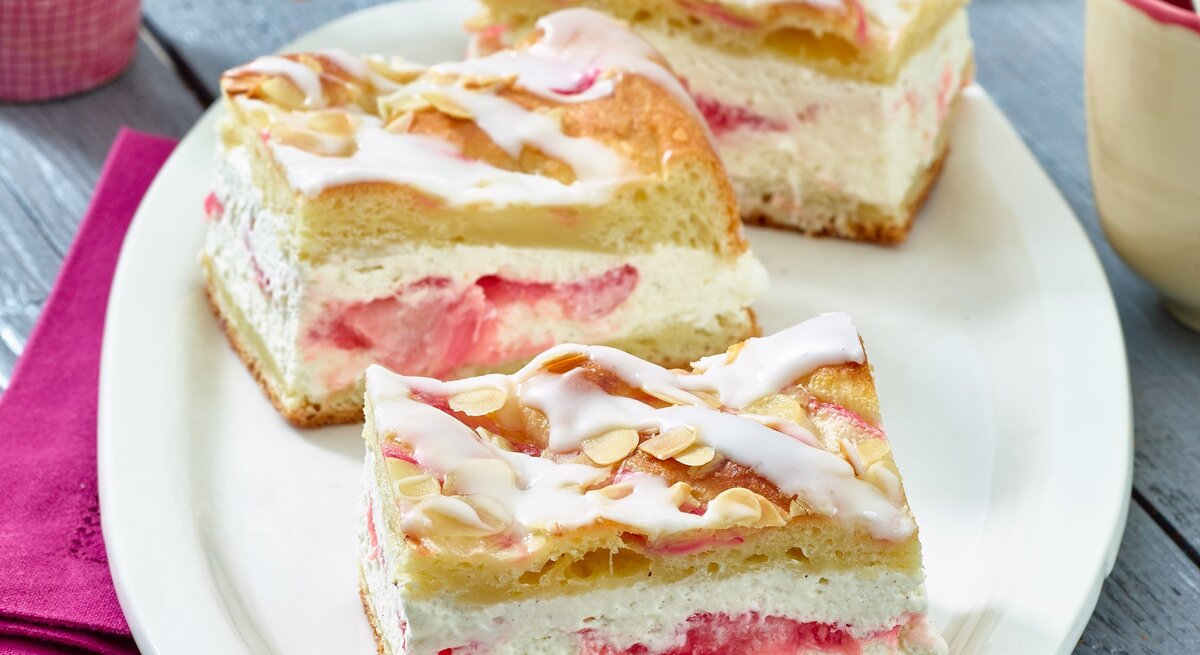 Auf einem ovalen hellen Teller aus Porzellan sind drei Stücke Rhabarber-Kuchen