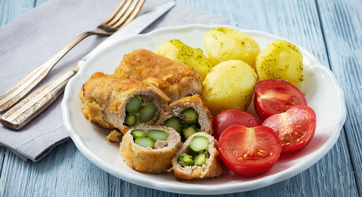 Schnitzel gefüllt mit Spargel zu Dill-Kartoffeln und Tomaten auf weißem Teller. 