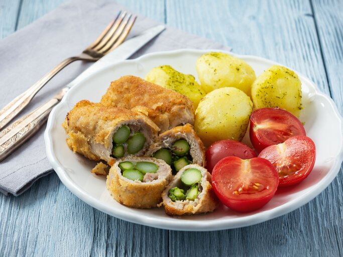 Schnitzel gefüllt mit Spargel zu Dill-Kartoffeln und Tomaten auf weißem Teller.  | © Getty Images/ Oleg Bannikov