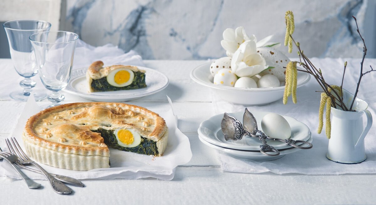 Eine angeschnittene Torta Pasqalina in weiß geschmücktem Ambiente, 