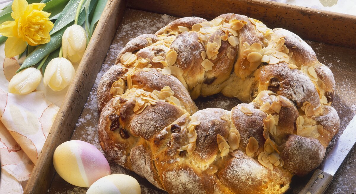 Der Osterkranz auf einem Holzbrett mit Oster-Deko im Hintergrund.
