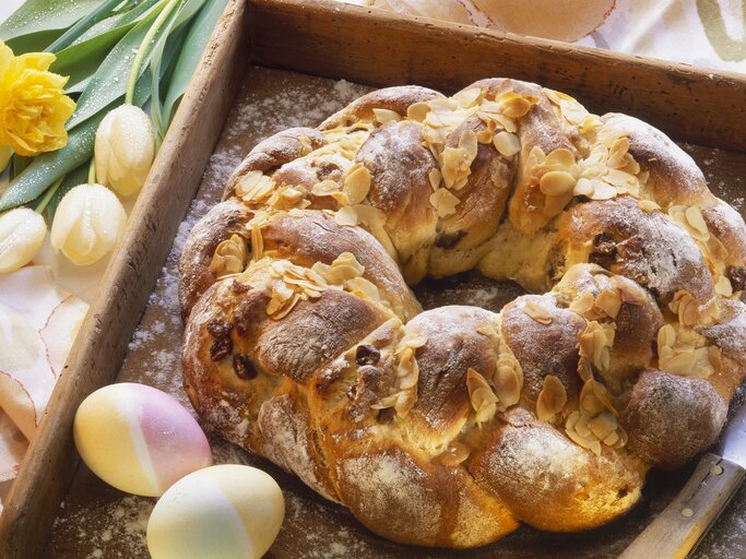 Der Osterkranz auf einem Holzbrett mit Oster-Deko im Hintergrund. | © StockFood / Harry Bischof