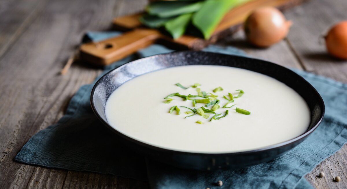 Ein schwarzer Suppenteller gefüllt mit einer cremigen, pürierten Lauchsuppe. 