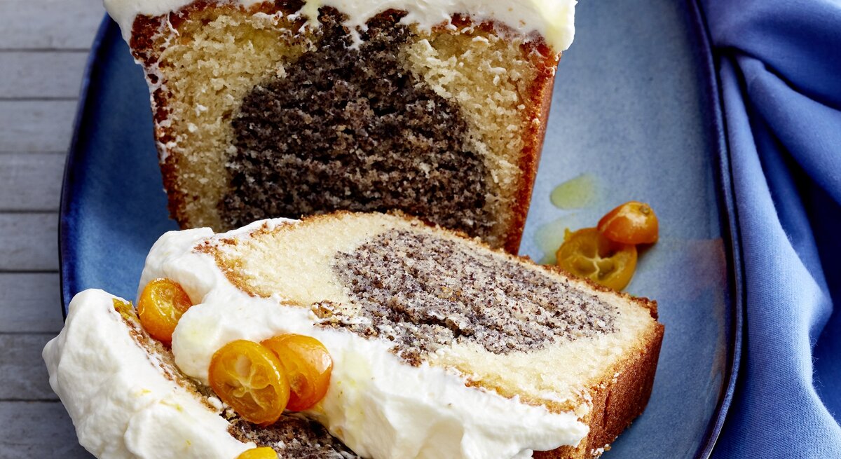 Mohn-Joghurt-Kuchen auf einem blauen Teller vor blauen Hintergrund. Rechts ein blaues Tuch. 