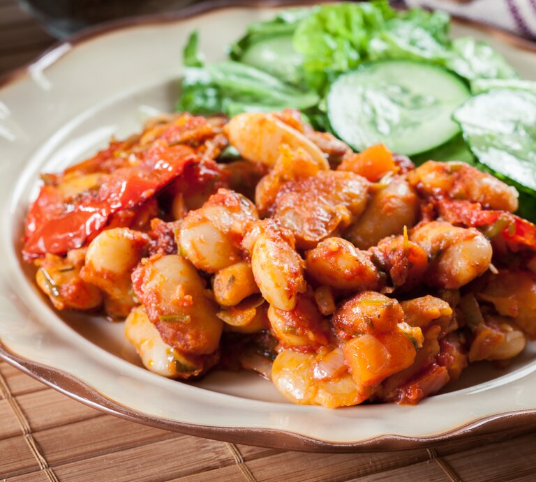 Weiße Bohnen in Tomatensoße mit Gurkensalat auf weißem Teller.  | © Shutterstock/Slawomir Fajer