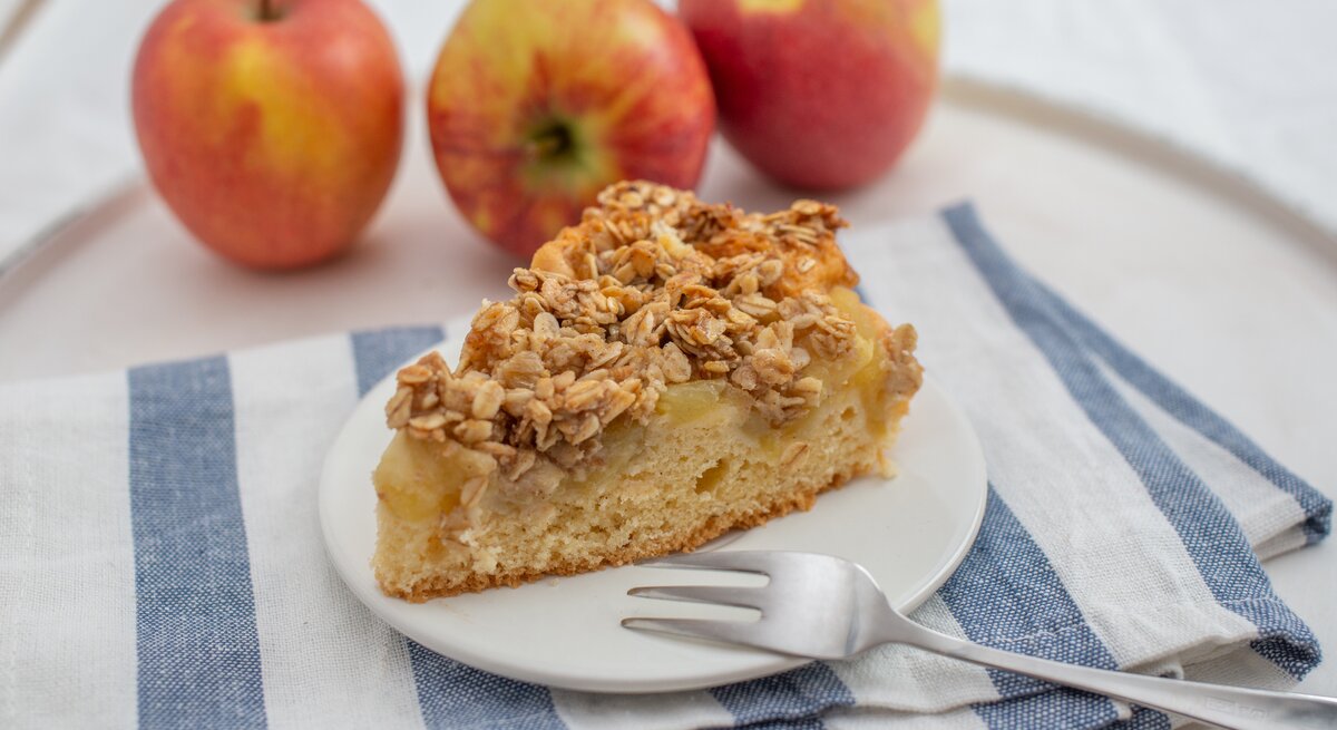 Ein Stück Apfelkuchen mit Haferflockentopping auf Teller.