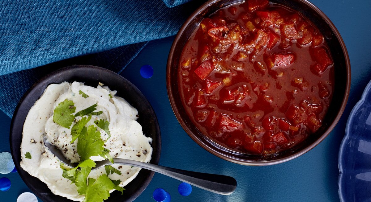 Paprika-Tomaten-Salsa in einer Schüssel, links daneben ein weiterer Dip. Der Hintergrund ist dunkelblau und darauf verteilt ein dunkelblaues Geschirrtuch.