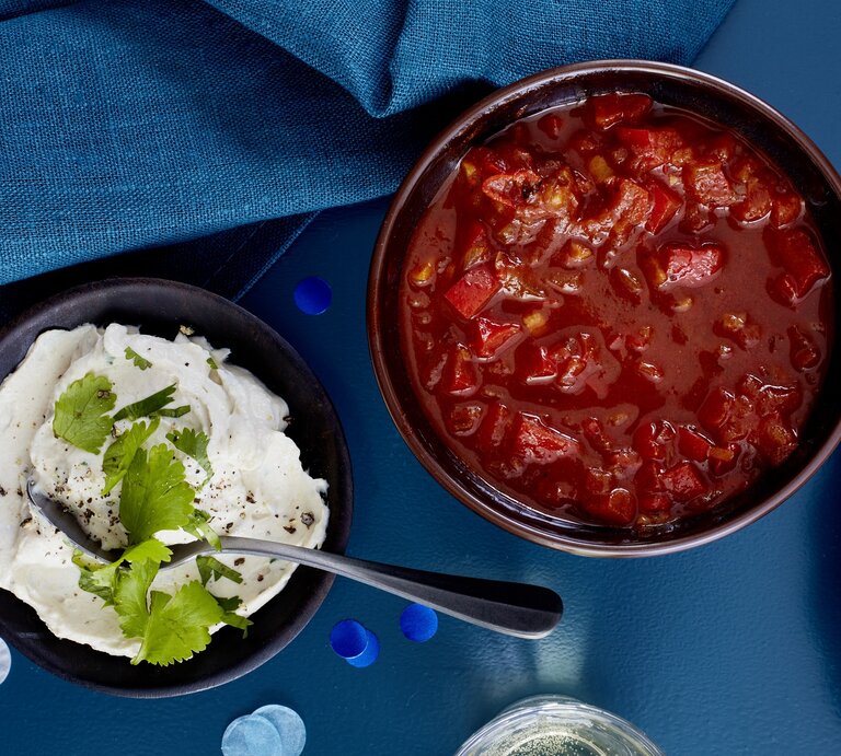 Paprika-Tomaten-Salsa in einer Schüssel, links daneben ein weiterer Dip. Der Hintergrund ist dunkelblau und darauf verteilt ein dunkelblaues Geschirrtuch. | © EAT CLUB/Isabell Triemer
