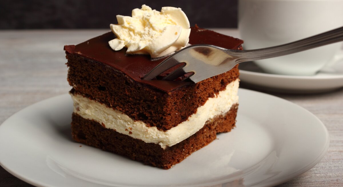 Geschichtete Schoko-Sahne-Torte mit Sahnehaube auf weißem Teller.