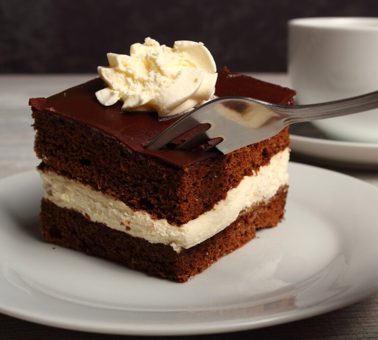 Geschichtete Schoko-Sahne-Torte mit Sahnehaube auf weißem Teller. | © Shutterstock/ffolas