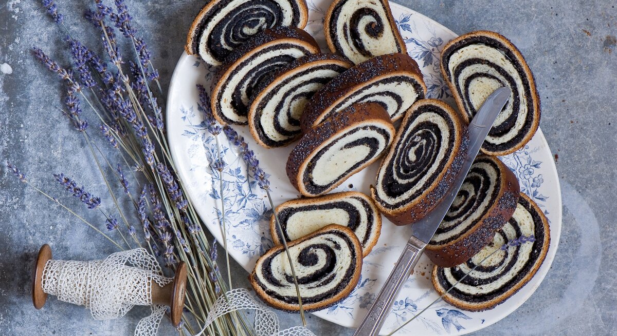 Der in Scheiben geschnittene Mohnstrudel auf einem dunkelblauen Teller und grauem Steintisch. Alles direkt von oben fotografiert.