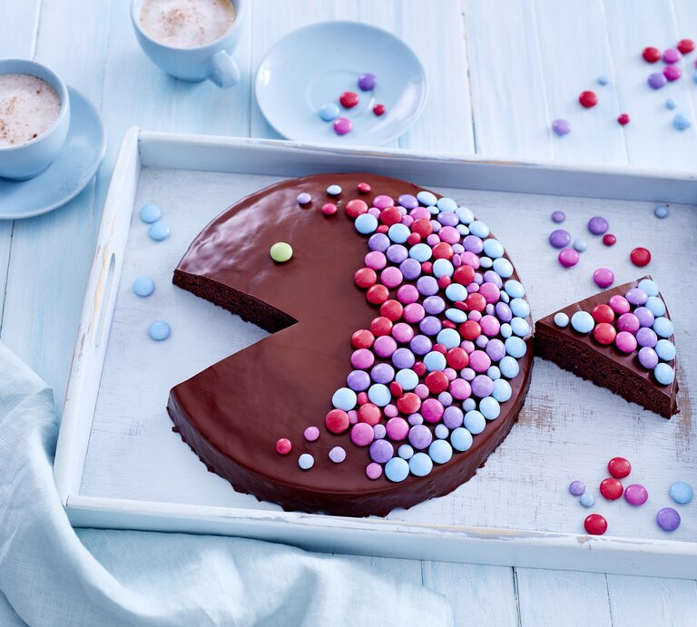Ein Schokoladen-Kuchen in Fischform der mit bunten Streuseln beleget ist auf einem hellblauen Untergrund und weißem Tablett von oben fotografiert. | © Eat Club; Isabell Triemer