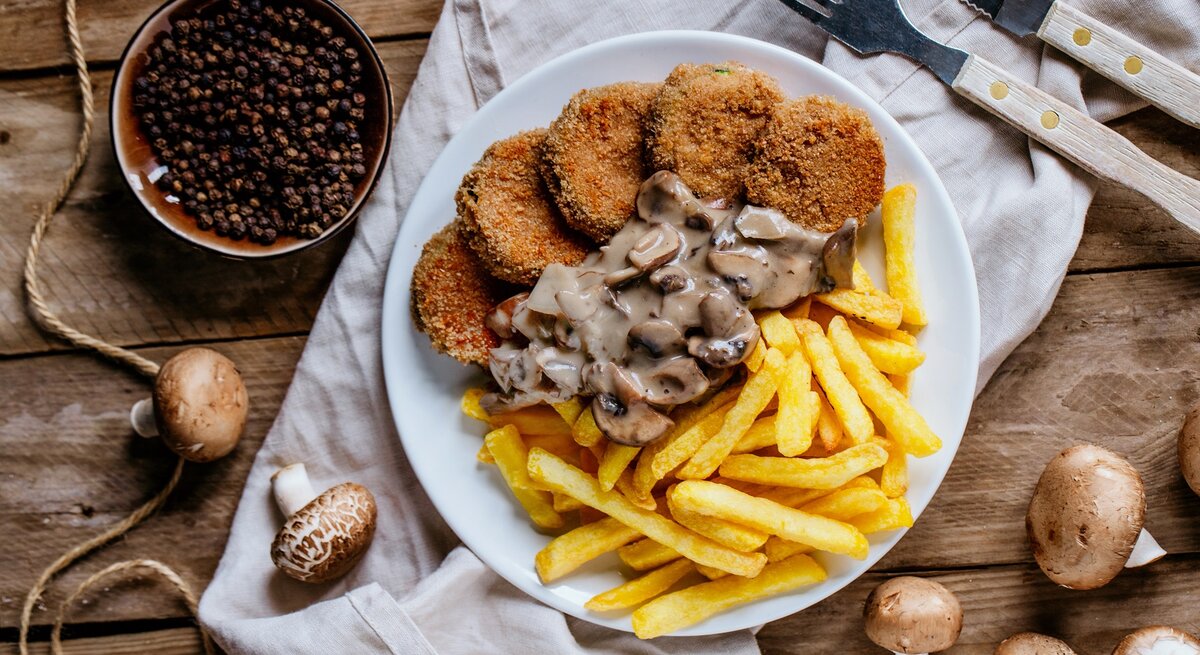 Jägerschnitzel mit Pilzsoße und Pommes / frische Pilze / Besteck / Küchentuch / Draufsicht