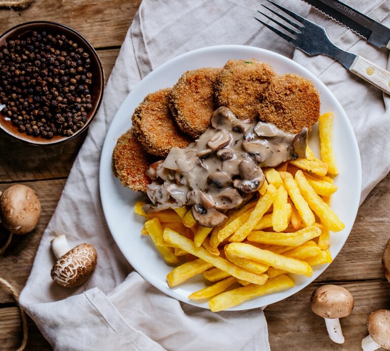 Jägerschnitzel mit Pilzsoße und Pommes / frische Pilze / Besteck / Küchentuch / Draufsicht | © PR