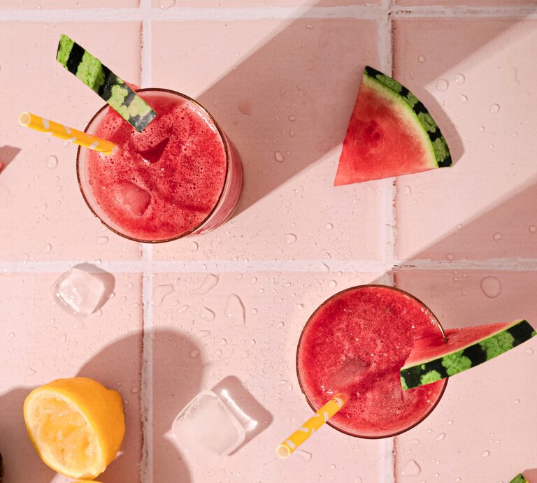Wassermelone Frosé in zwei großen Gläsern mit Strohhalm und frischer Melone auf einem rosa Tisch aus Fliesen.  | © Getty Images / Flavia Morlachetti