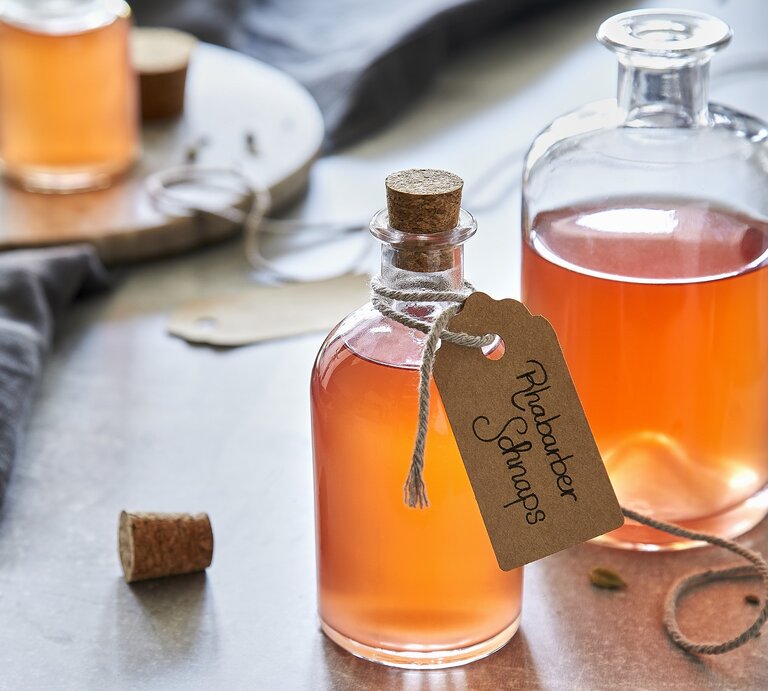 Draufsicht schräg: Drei Flaschen aus Glas in denen eine Flüssigkeit ist. Um eine Flasche hängt ein kleines Papierschild, auf dem "Rhabarberschnaps" geschrieben steht. | © StockFood/Springlane