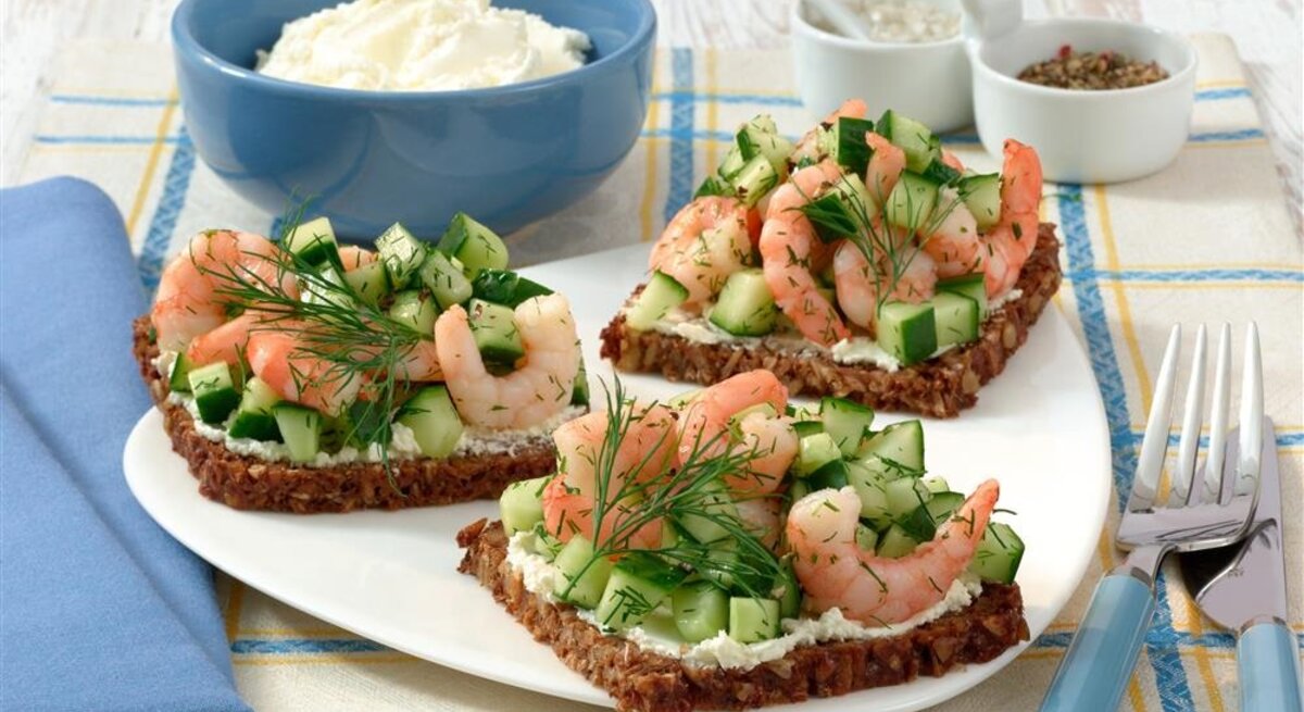 Drei Scheiben Vollkornbrot mit Frischkäse, Gurken und Garnelen.