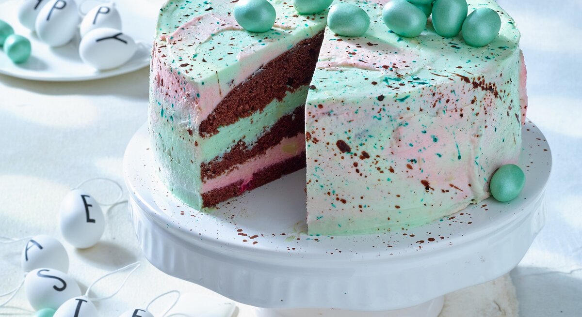 Waldmeister-Himbeer-Torte: Ostertorte mit grünlicher Creme und Schokoeiern auf einem weißen Servierteller.