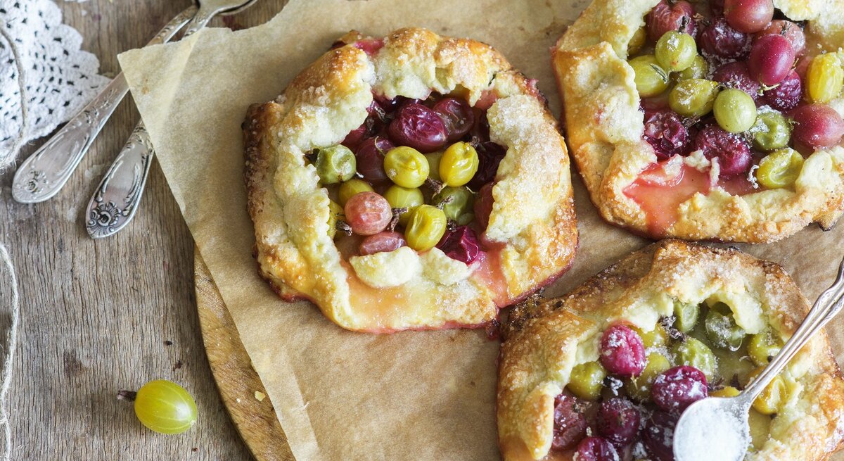 Drei kleine Stachelbeerkuchen auf einem Blech mit Backpapier direkt von oben fotografiert.