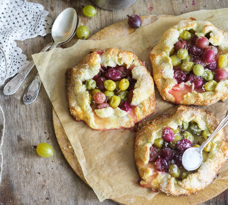 Drei kleine Stachelbeerkuchen auf einem Blech mit Backpapier direkt von oben fotografiert. | © StockFood / Meliukh, Irina