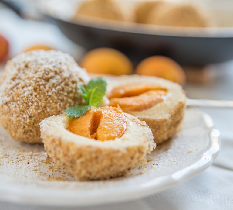 Zwie angeschnittene Marillenknödel auf einem hellen Teller nah und von vorne fotografiert. | © iStock/A_Lein