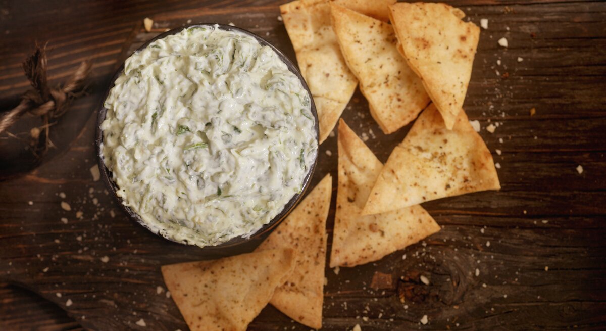 Draufsicht auf einen Artischocken-Spinat-Dip. Daneben einige Nachos.