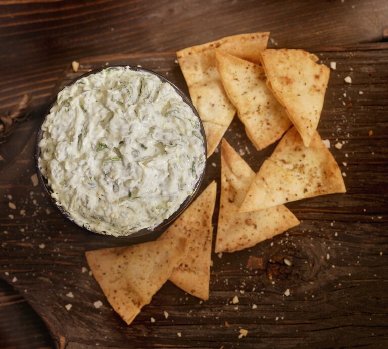 Draufsicht auf einen Artischocken-Spinat-Dip. Daneben einige Nachos. | © iStock/ LauriPatterson